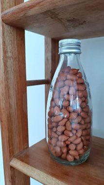 Fıstıkla dolu cam bir şişe ahşap bir rafta duruyor. Şişenin yarısı dolu ve fıstıklar şişeye saçılmış. Bolluk ve bolluk kavramı.