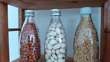 Farklı türde ceviz ve tohumlarla dolu üç cam şişe. Şişeler ahşap bir rafta.