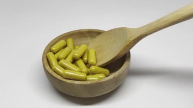 Sarı kapsüllerle dolu ahşap bir kase, muhtemelen beslenme takviyesi ya da ilaç..