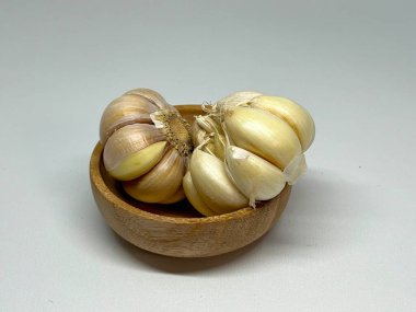 Tarafsız bir arkaplanda tahta bir kasede iki sarımsak soğanı..