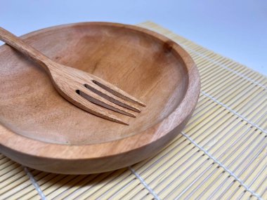 Bambu hasırı üzerinde ahşap bir kase ve çatal, yemek servisi ya da yemek için uygundur..