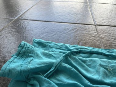 A wrinkled turquoise shirt casually draped on glossy floor tiles clipart