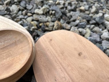 Küçük çakıl taşlarından bir yatakta dinlenen iki ahşap servis tabağı..