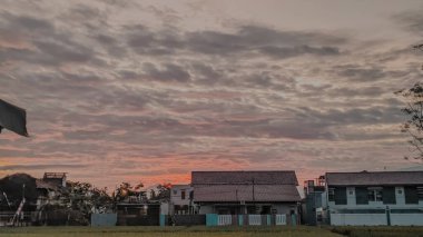 Bulutlu ve renkli bir yerleşim yerinin üzerinde huzurlu bir günbatımı.