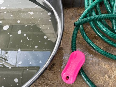 Yeşil bir hortum ve pembe bir temizliğin yanında bir kova sabunlu su. 