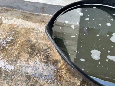 Bulanık suyla dolu siyah bir kase, ışığı ve sörfü yansıtıyor.