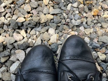 Küçük çakıllardan oluşan bir yatakta dinlenen siyah ayakkabıların yakın çekimi. 