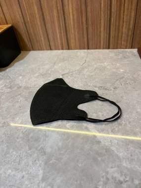 Kişi için tasarlanmış gri bir yüzeyde duran siyah bir yüz maskesi.