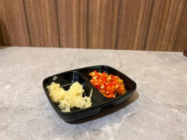 İçinde dilimlenmiş sarımsak ve acılı biber olan küçük siyah bir yemek.