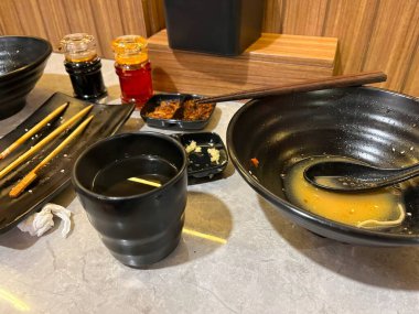 Boş kaseler, yemek çubukları ve baharatlarla dolu bir yemek masası.