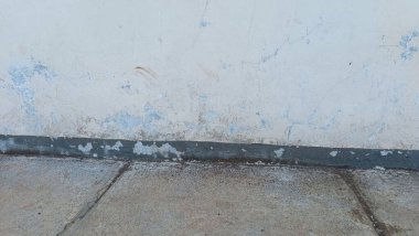 Soyulmuş boya ve beton dokusunu gösteren yıpranmış bir duvar ve zeminin yakın çekimi..