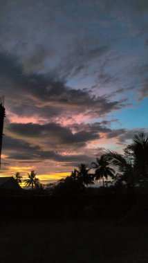 Canlı bir günbatımı. Renkli bulutlar ve palmiye ağaçlarının siluetleri..