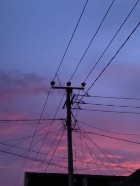 Renkli bir günbatımı gökyüzüne karşı elektrik hatlarının ve elektrik direğinin silueti..
