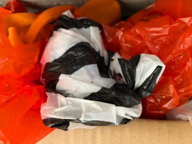 Bir resim, atık veya geri dönüşüm kavramlarını göstermek için ideal siyah, beyaz ve turuncu plastik torbalar yığınını gösterir.