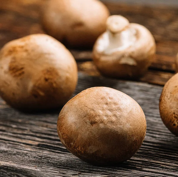 stock image Several fresh champignons mushrooms on old wooden background, selective focus