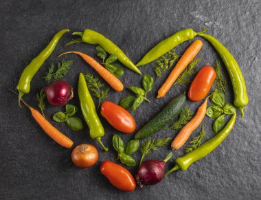 Taze mevsimlik sebzelerden yapılmış kalp: yeşil biber, domates, soğan, havuç, salatalık, fesleğen, dereotu gri arka planda, üst manzara, stok fotoğrafı