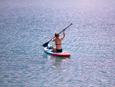 Villach, Austria - 2022 September 4 : Young blonde woman  paddling a canoe on a scenic lake on a summer afternoon, Faaker See