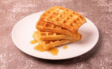 Delicious Belgian waffles with honey served on white plate and brown background, rustic concept.