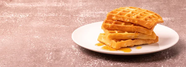 Delicious Belgian waffles with honey served on white plate and brown background, rustic concept, space for text