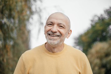 Sarı kazaklı neşeli yaşlı adam Verdant Urban 'da gülüyor.