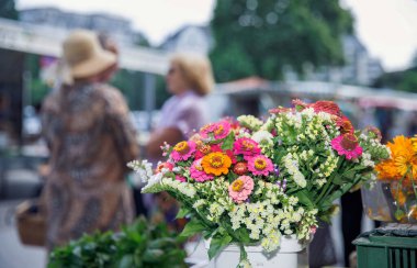 Villach, Avusturya - 07.13.2024: Arka planda bulanık insanlarla birlikte açık hava pazarında canlı, taze çiçek buketlerinin sergilenmesi, pazar tezgahı kavramı