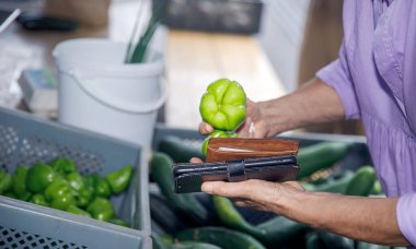 Villach, Avusturya - 07.13.2024: Bir müşteri, yerel bir markette cüzdan tutarken yeşil bir dolma biberi inceliyor, taze sebze kavramı