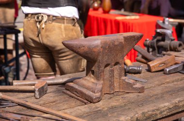 Ahşap tezgahta paslı örs, demirci aletleri açık hava atölyesi ortamında yayılmış, geleneksel metal çalışma konsepti.