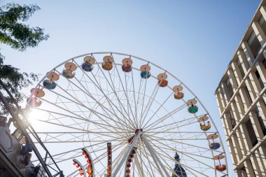 Bir lunaparkta dönme dolap, açık mavi bir gökyüzü altında, boş zamanları ve aydınlık, güneşli bir günü temsil eder.
