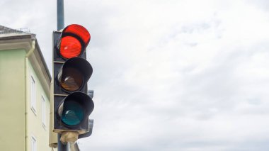 Bulutlu gökyüzünün altındaki kavşakta kırmızı, sarı, yeşil sinyalli trafik ışığı, şehir güvenliği kavramı