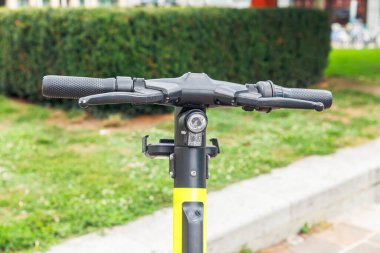 Yeşil park arka planına sahip modern elektrikli scooter 'ın gidonunun yakın görüntüsü, kentsel ulaşım kavramı