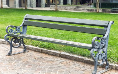 Yeşil bir parkın kaldırım taşı yolunda boş bir banka, arka planda yeşil çimenler ve ağaçlara bakıyor, şehir dışı rahatlama, kamu oturma konsepti