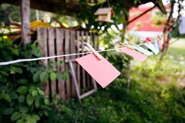 Renkli kağıt kartlar, iple asılı, mandallar, bahçe arka planı, yaz günü, köy sahnesi, iletişim ve dekor konsepti.