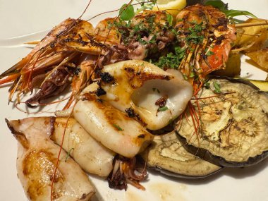 Beyaz tabakta ızgara deniz ürünleri, kalamar, karides ve patlıcan.