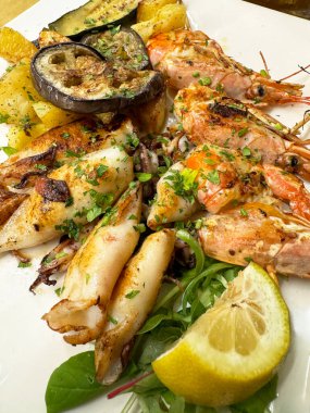 Limonla süslenmiş karides, kalamar ve sebzeli ızgara deniz ürünleri tabağı.