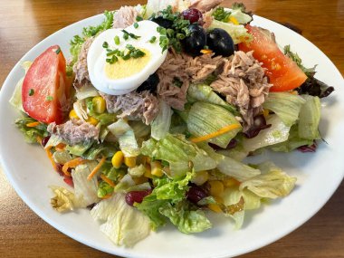 Beyaz tabakta haşlanmış yumurta ve sebzeli ton balığı salatası.