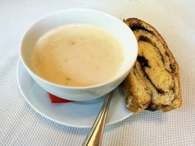 Kremalı çorba ve beyaz tabakta bir dilim girdaplı ekmek.