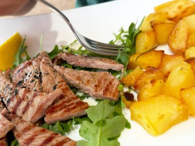 Sulu ızgara biftek ve limon dilimli roka üzerinde altın patates.