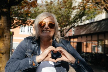 Güneş gözlüklü mutlu kadın açık havada kalp hareketi yapıyor.