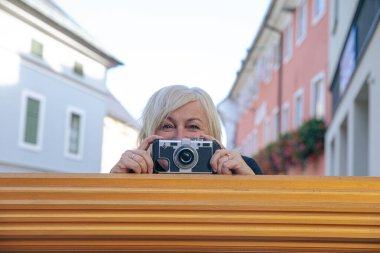 Şehir ortamında elinde klasik kamera tutan gülümseyen kadın.