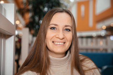 Modern bir binada uzun kahverengi saçlı, gülümseyen bir kadın.