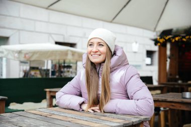 Kış kıyafetli gülümseyen kadın açık hava kafe ortamında eğleniyor.