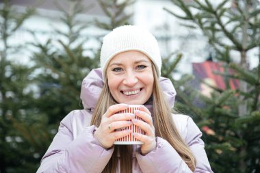 Kışlık ceketli mutlu kadın doğada sıcak içkinin tadını çıkarıyor.