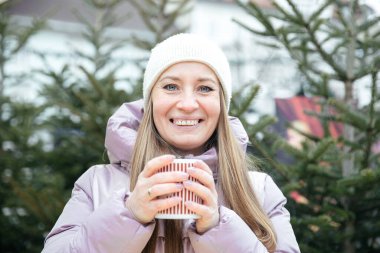 Gülümseyen kadın, kışın harikalar diyarında sıcak içkinin tadını çıkarıyor.