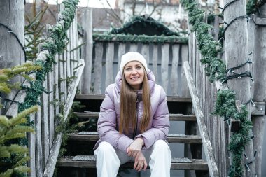 Kışın gülümseyen kadın dışarıdaki süslü ahşap merdivenlerde oturuyor.