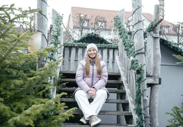 Kışlık giysiler içinde gülen kadın kırsal ahşap merdivenlerde dinleniyor.