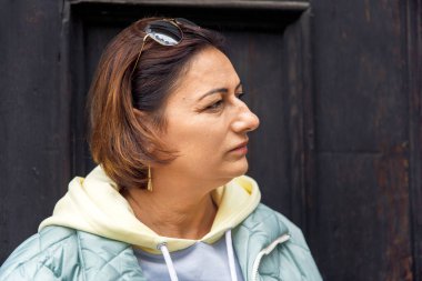 Güneş gözlüklü, koyu renk arka planda düşünceli bir kadın.