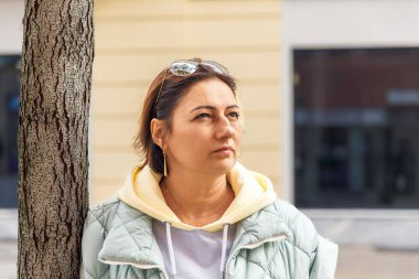 Şehir ortamında güneş gözlüğü ve günlük kıyafet takan düşünceli bir kadın.