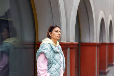 Örtülü ceketli bir kadın kemerli mimaride geziniyor.