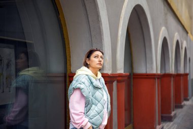Pastel giyimli kadın kemerli geçitle şehir mimarisini keşfediyor.