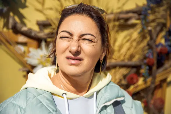Parlak güneş ışığında şaşı bakan bir kadın, doğal arka planda.